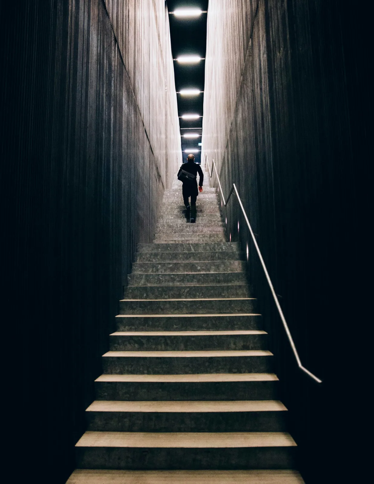 Person walking up a long narrow staircase toward overhead lights