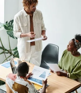 Three colleagues reviewing charts and documents around a meeting table