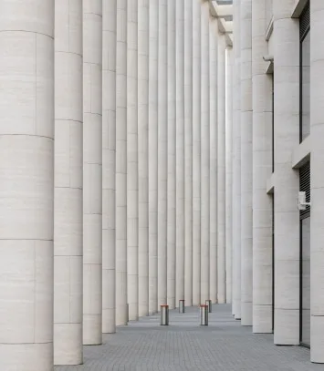 Perspective view of a long colonnade of tall cylindrical columns along a paved walkway